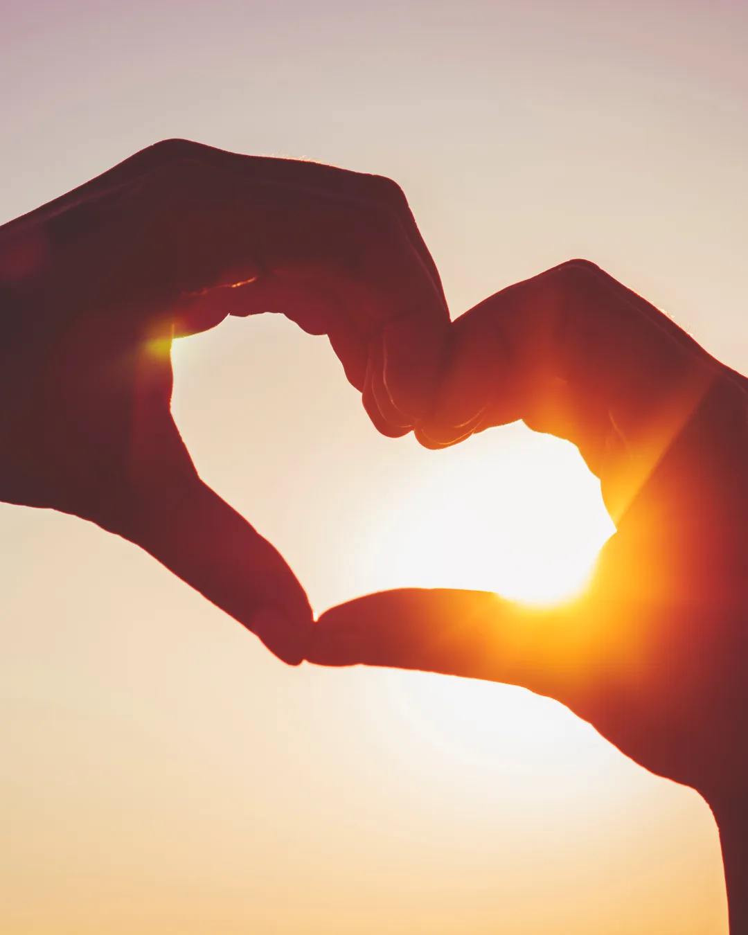 Hands forming a heart shape against a sunset